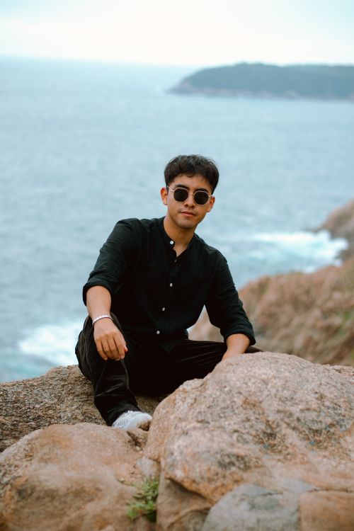Free A man in black sits on a rocky cliff with a scenic ocean background in Oaxaca. Stock Photo