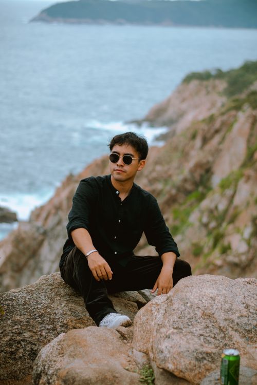 Free Young man in sunglasses sitting on rocks with a view of the Huatulco coastline, Oaxaca, Mexico. Stock Photo