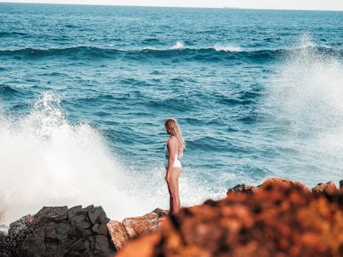 Woman in White Swimsuit Standing on Rock by the Sea