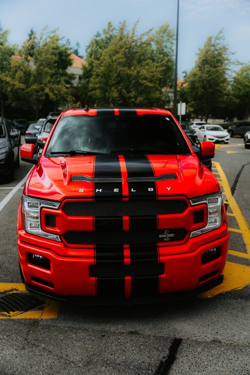 Free Front view of a striking red Shelby performance truck in a parking lot, surrounded by trees. Stock Photo