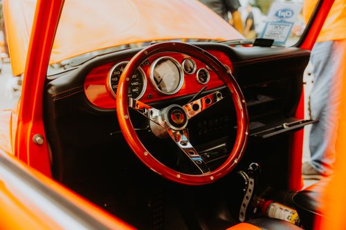 Free Vibrant red classic car interior showcasing a polished wooden steering wheel and vintage dashboard. Stock Photo
