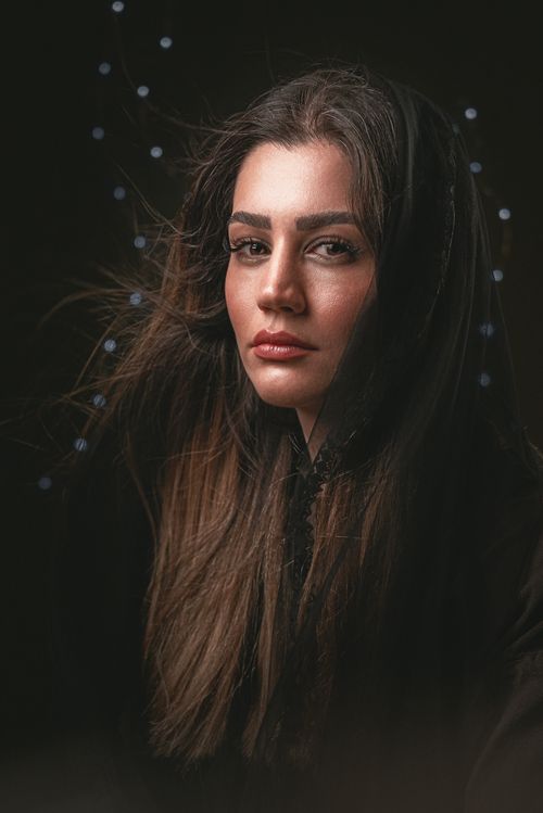 Free Artistic portrait of a woman with long dark hair and intense gaze under a hood on a dark background. Stock Photo
