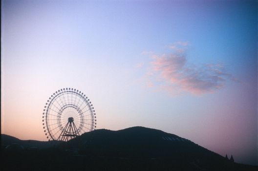 Silhouette of a Ferris wheel against a colorful twilight sky.
