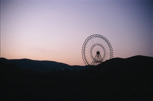 Silhouette of a Ferris wheel against a pastel sunset sky over hills.