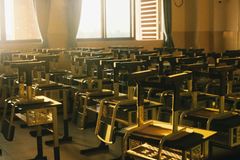 Sunlit empty classroom with chairs stacked on desks, warm and serene atmosphere.