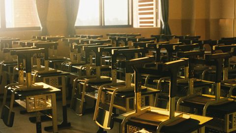 Sunlit empty classroom with chairs stacked on desks, warm and serene atmosphere.