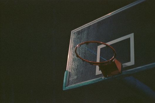 A dimly lit basketball hoop captured at night with an atmospheric feel.