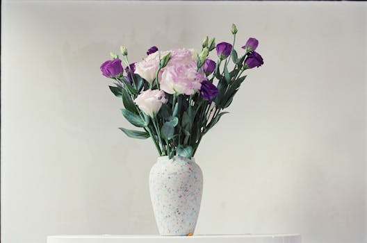 A minimalist display of pink and purple flowers in a ceramic vase on a white stand.