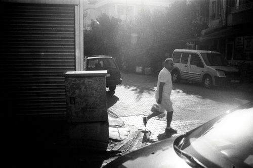 Free Black and white photo of a man walking on a sunlit street corner. Stock Photo