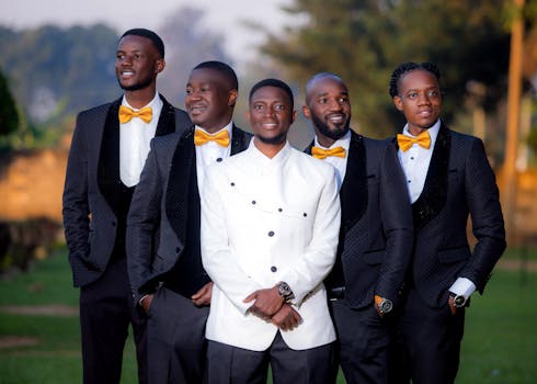 Five men in suits with yellow bow ties posing outdoors, smiling confidently.