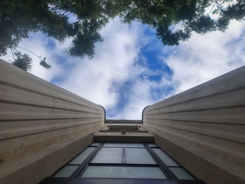 Free Dramatic perspective of a building's facade reaching towards a cloudy sky with tree branches framing the view. Stock Photo