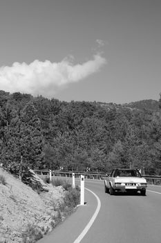 Vintage car driving on winding mountain road in black and white setting.