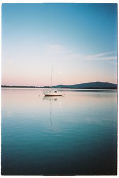 Sailing boat on tranquil lake water with mountain backdrop during dusk.