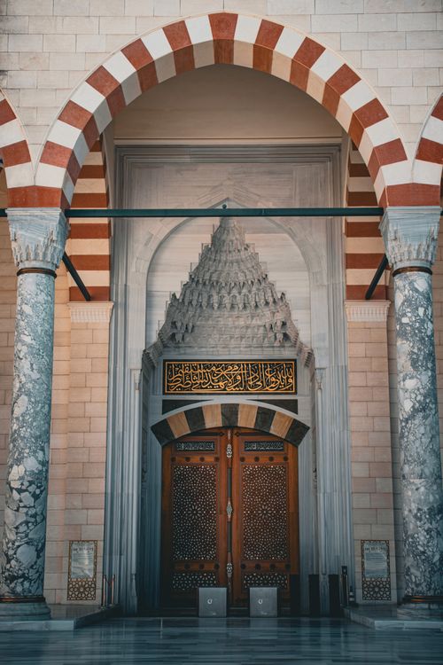 Free Detailed view of a mosque entrance with Islamic architecture, arches, and Arabic calligraphy. Stock Photo