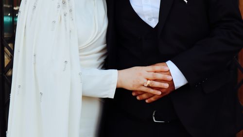 Free Close-up of a couple holding hands dressed in elegant formal attire, symbolizing unity and love. Stock Photo