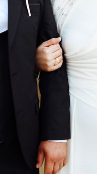 Close-up of a bride and groom holding arms, showcasing elegant wedding attire and jewelry.