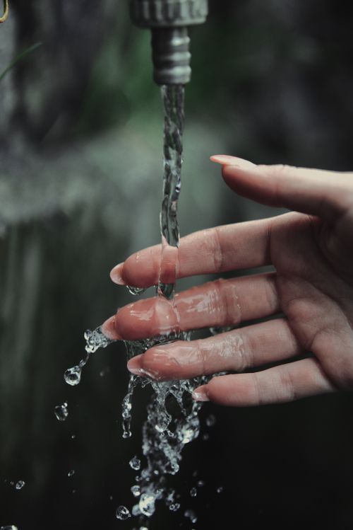 Free A woman's hand under flowing water from an outdoor faucet, capturing the motion and freshness. Stock Photo