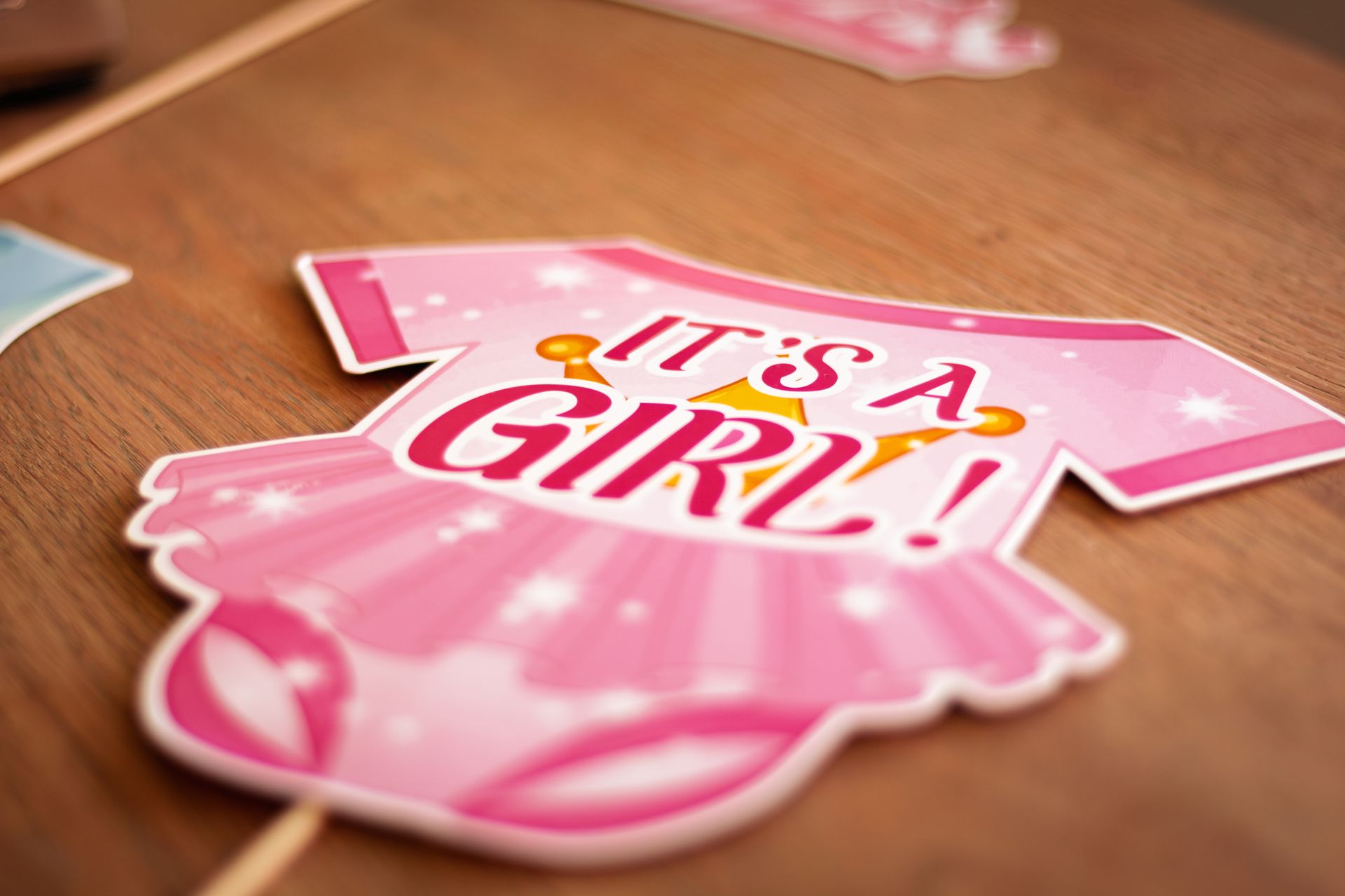 Pink 'It's a Girl' baby shower sign on a wooden surface capturing a joyful announcement theme.
