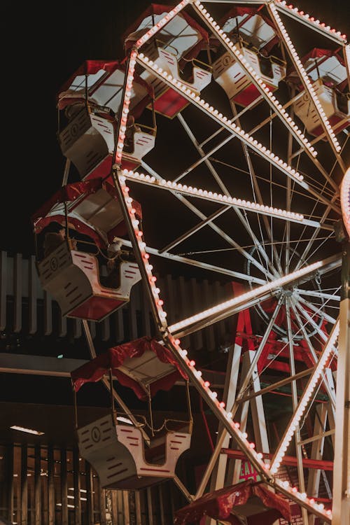 From below of round illuminated Ferris wheel in amusement park against dark night sky