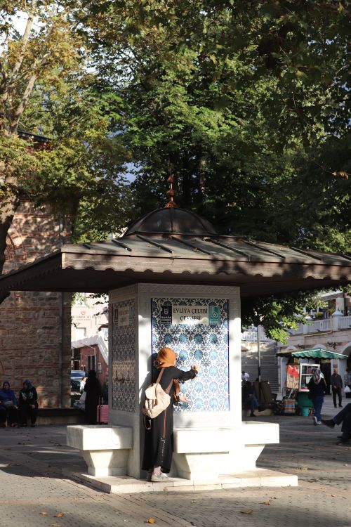 Free Woman wearing headscarf at a historical Ottoman-style fountain surrounded by trees in urban park. Stock Photo