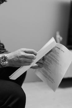 Close-up of a man reading documents, focus on hand and watch in a professional setting.