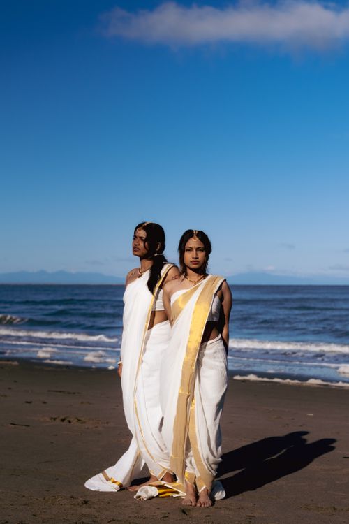 Free Two women wearing traditional sarees pose gracefully on a Vancouver beach at sunrise, showcasing cultural fashion. Stock Photo