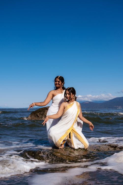 Free Two women in traditional sarees pose gracefully on a Vancouver beach under a clear blue sky. Stock Photo