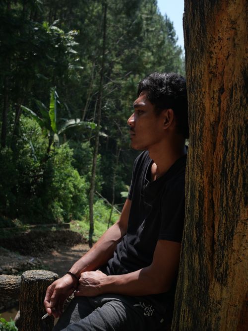 Free Man enjoying the tranquility of a lush forest setting, leaning against a tree. Stock Photo