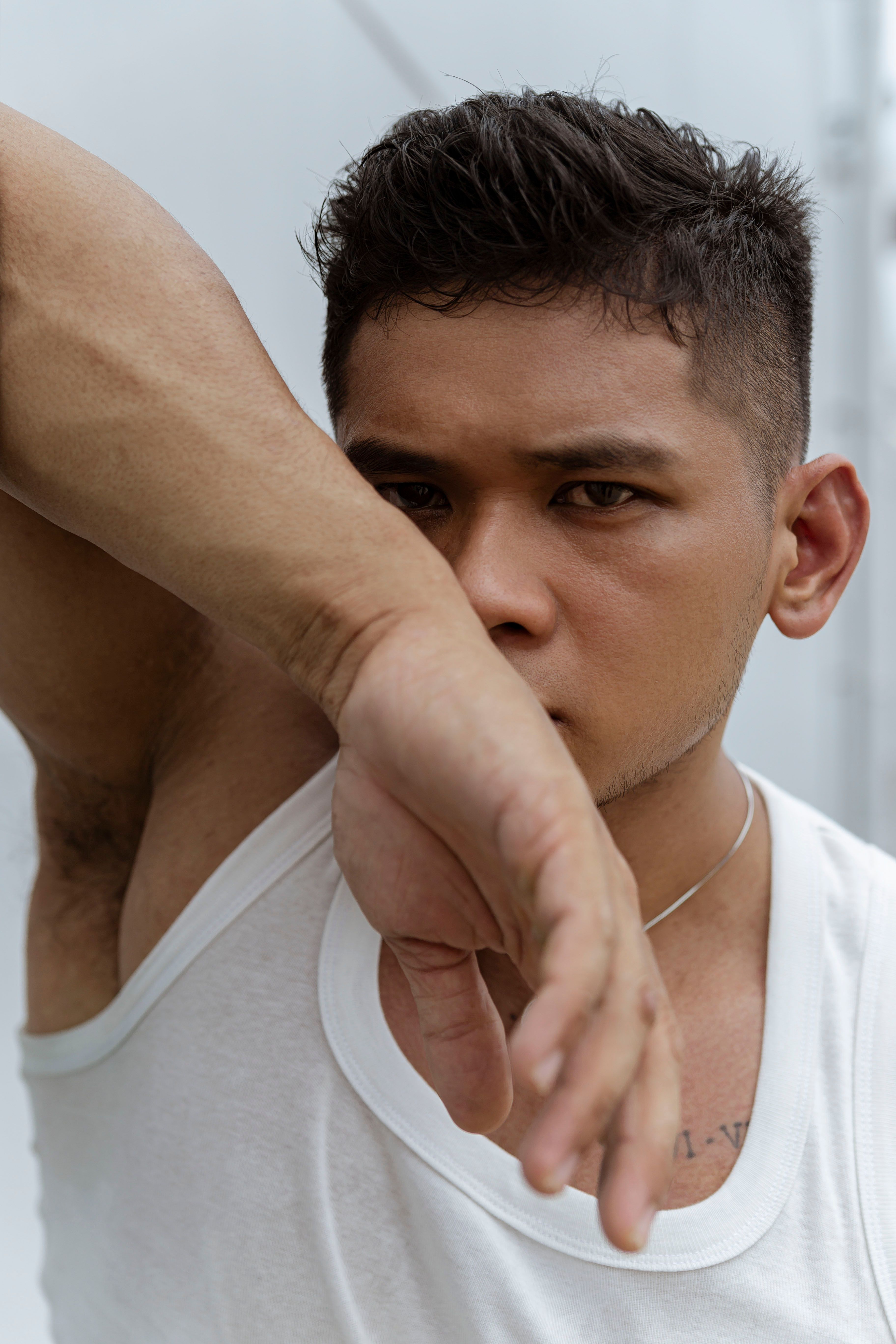 Close-up portrait of a young man in a white tank top, gazing intensely.
