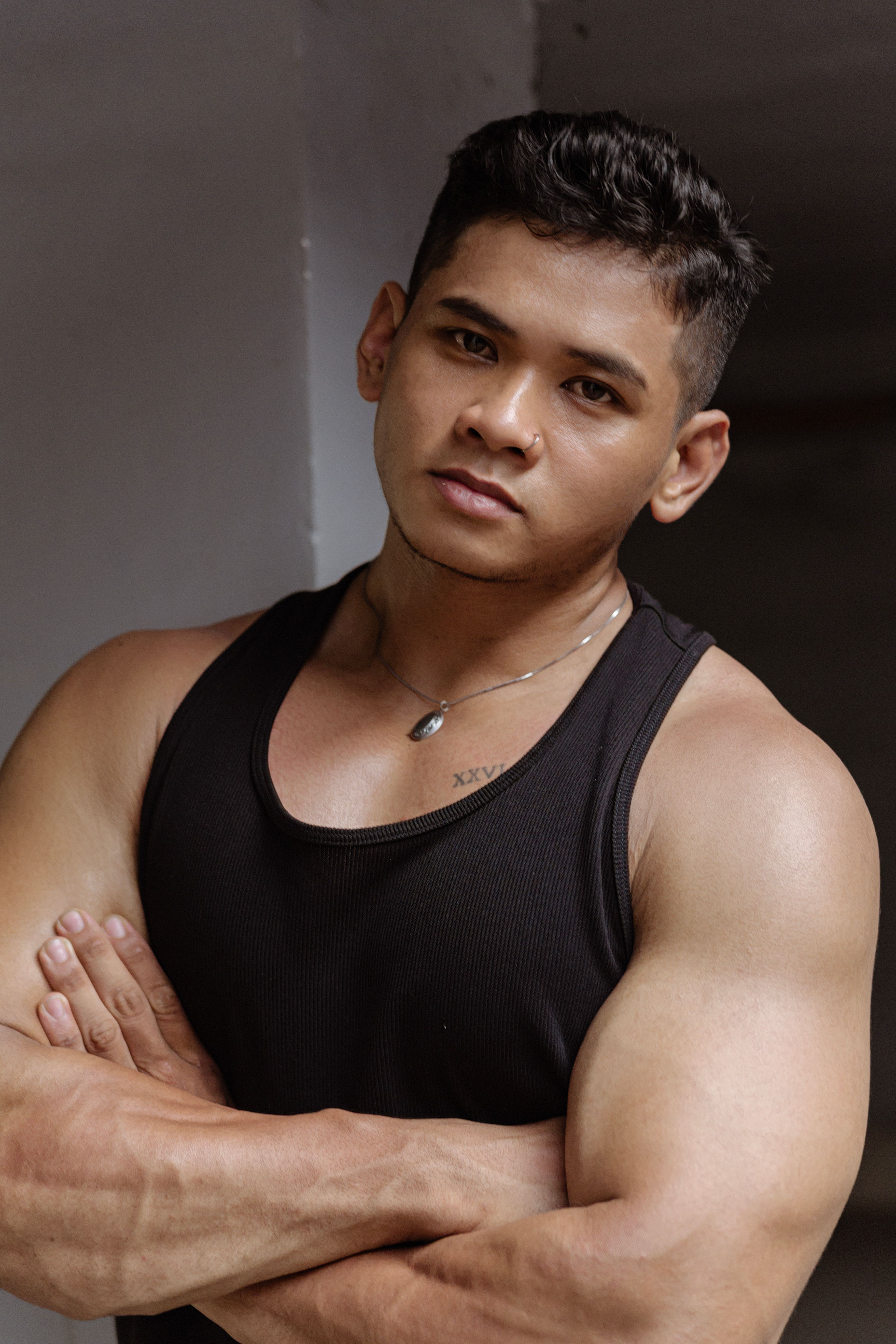A muscular young man posing confidently in a black tank top indoors.