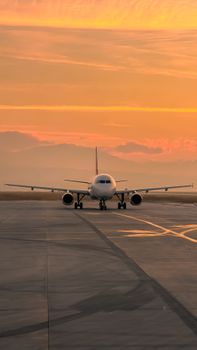 A passenger airplane on a runway during a scenic golden sunset, captured from the front.