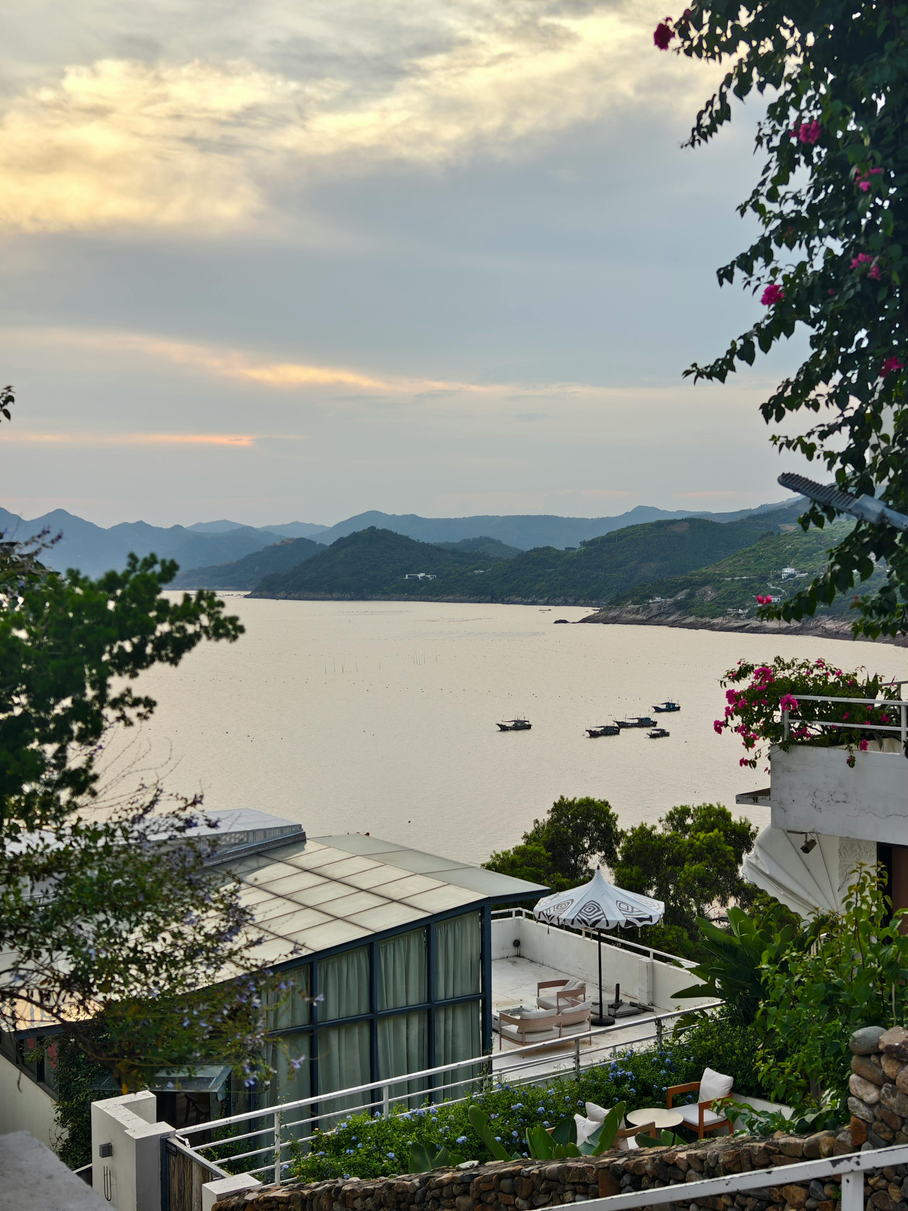 A stunning sunset view over a peaceful coastal landscape, framed by lush greenery and elegant architecture.
