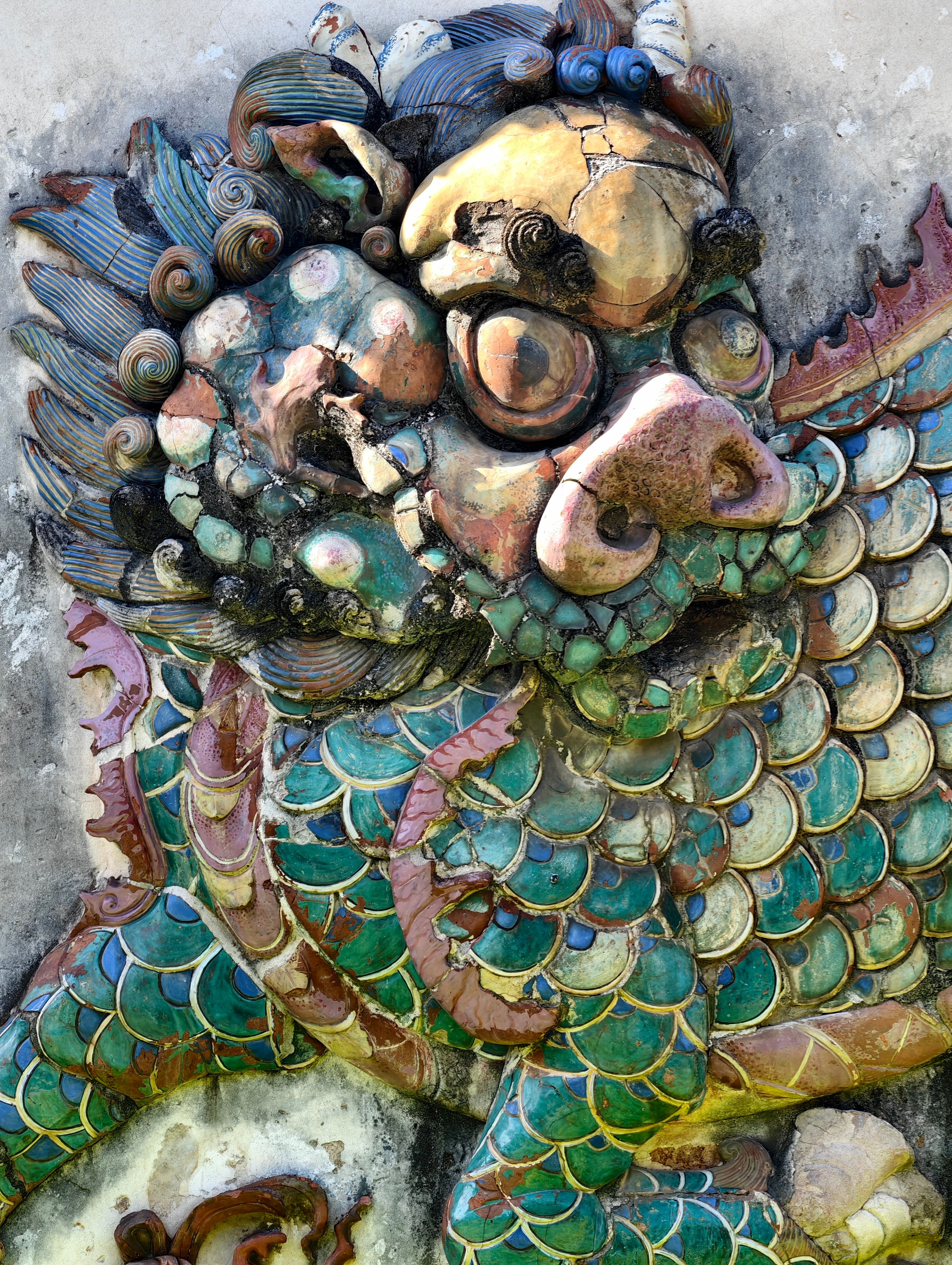 Vibrant ceramic dragon sculpture with intricate details and visible cracks.