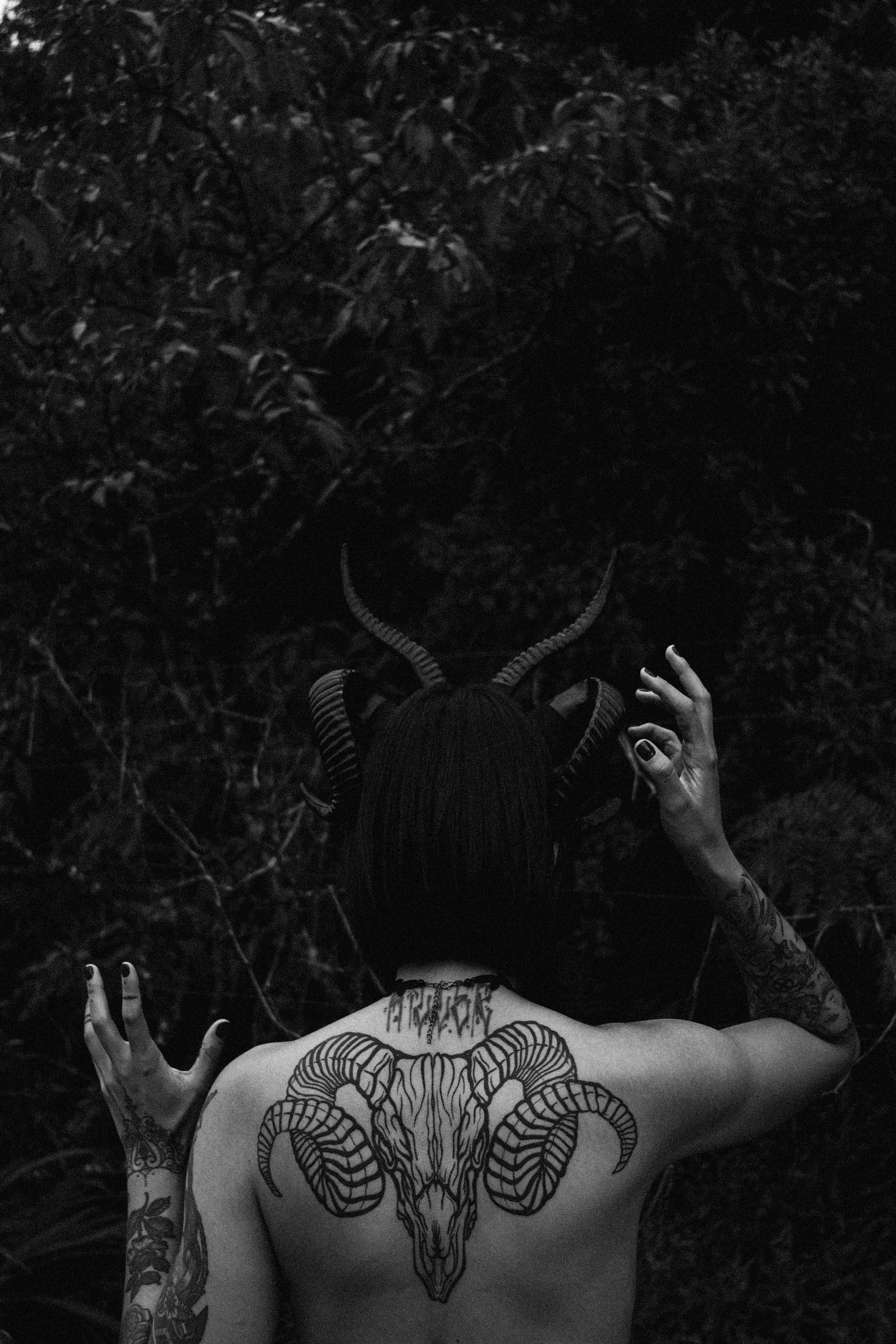 Gratuit Une personne mystique avec une coiffe à cornes et des tatouages pose dans une forêt sombre. Photos
