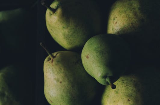 A close-up shot of fresh green pears with a moody lighting effect, highlighting their texture.