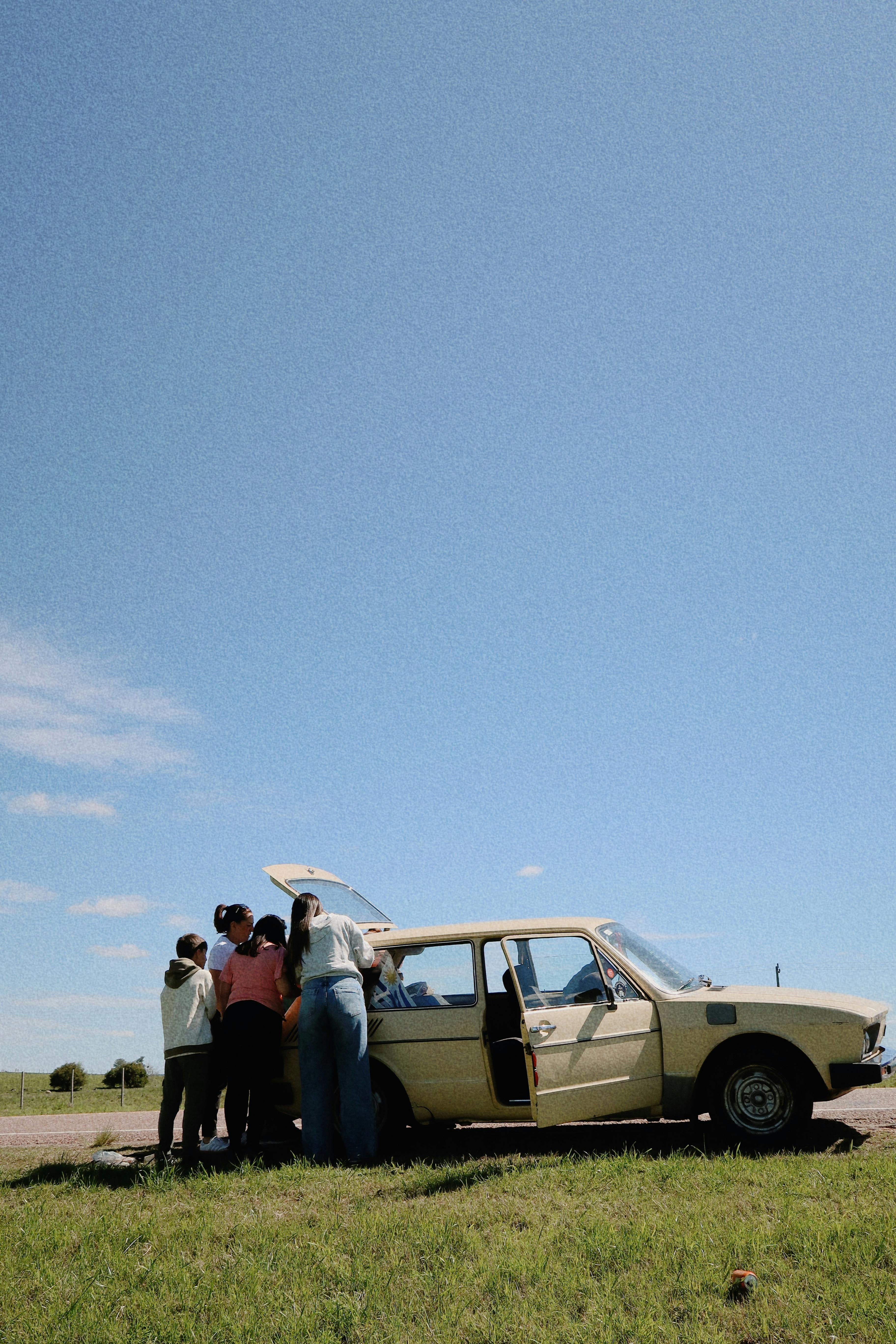 A group enjoying a road trip by a vintage car on a sunny day in Melo, Uruguay.