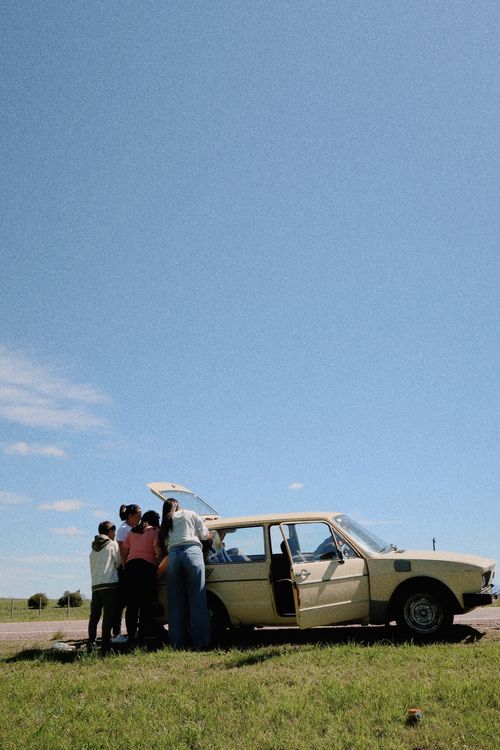 Free A group enjoying a road trip by a vintage car on a sunny day in Melo, Uruguay. Stock Photo