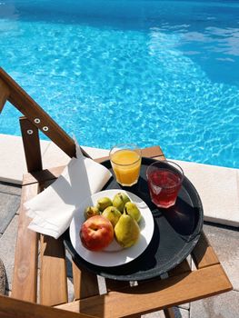 Poolside tray with fresh fruits and drinks on a sunny day, perfect summer relaxation.