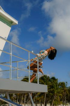 An elegant woman in floral attire poses confidently on a balcony against a tropical backdrop.