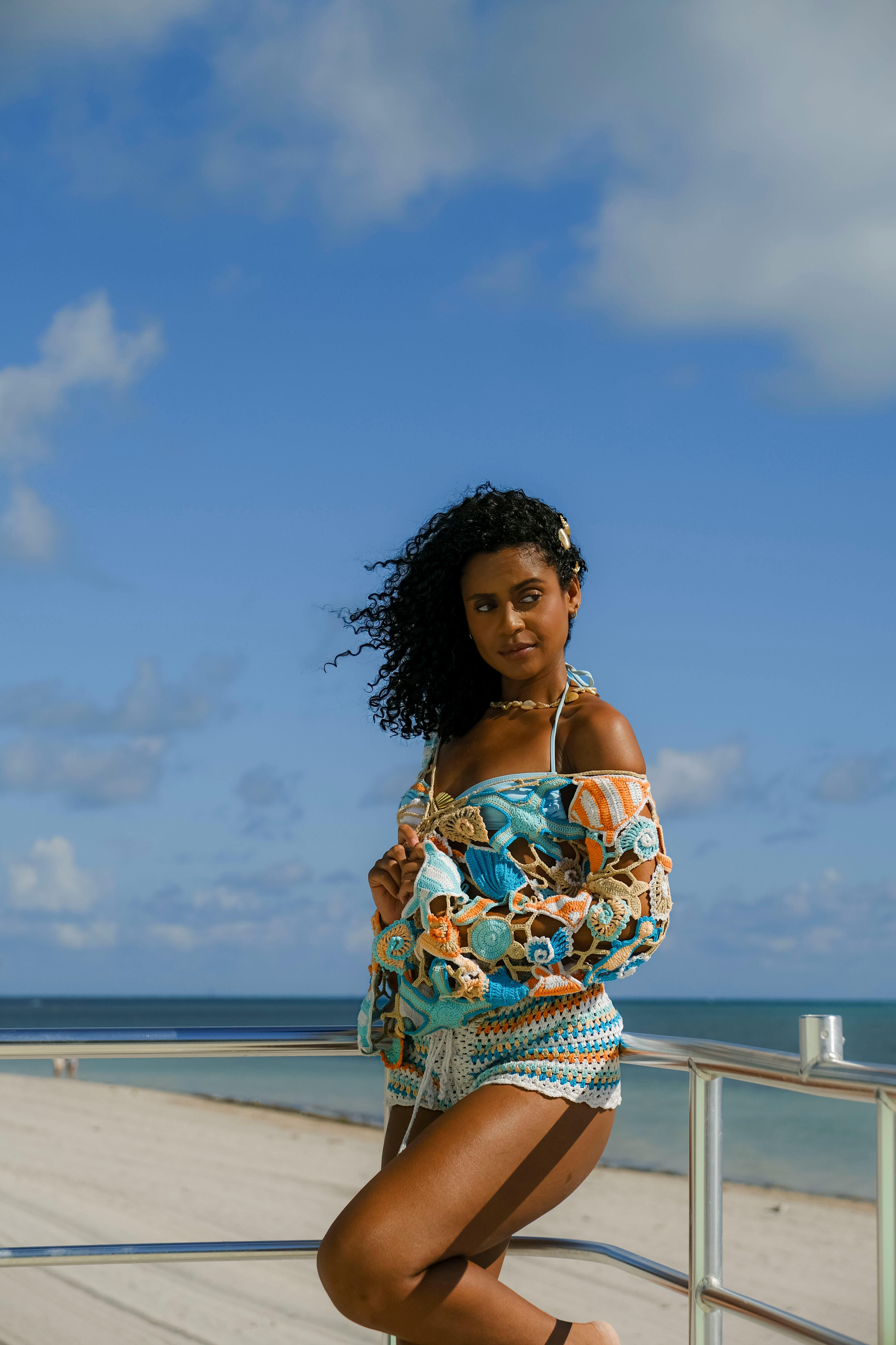 Free Woman in colorful dress poses confidently on a beach under a clear sky. Stock Photo