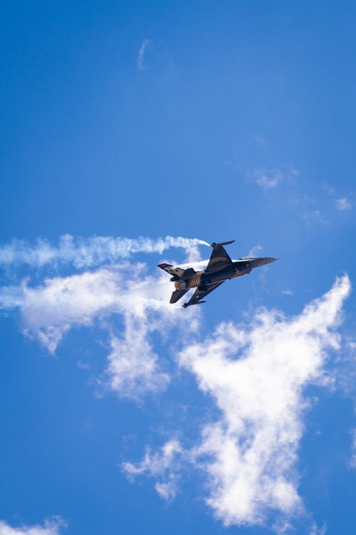 Free A powerful jet fighter executes a skillful aerial maneuver against a backdrop of clear blue skies and wispy clouds. Stock Photo