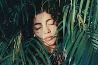 一幅宁静的肖像画，一位闭着眼睛、被绿色棕榈叶包围的女人