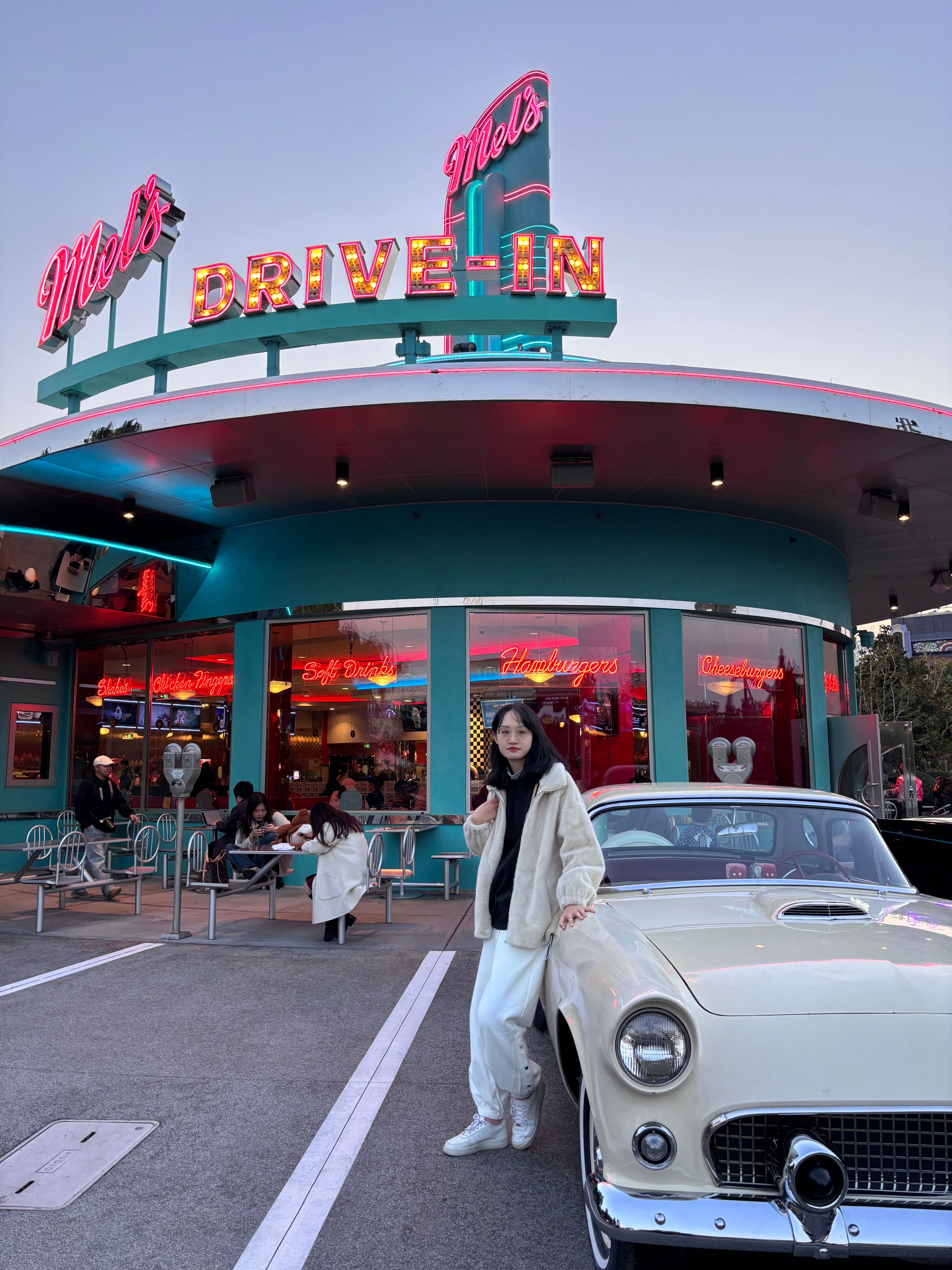 Retro drive-in diner scene with a vintage car and patrons enjoying the evening ambiance.