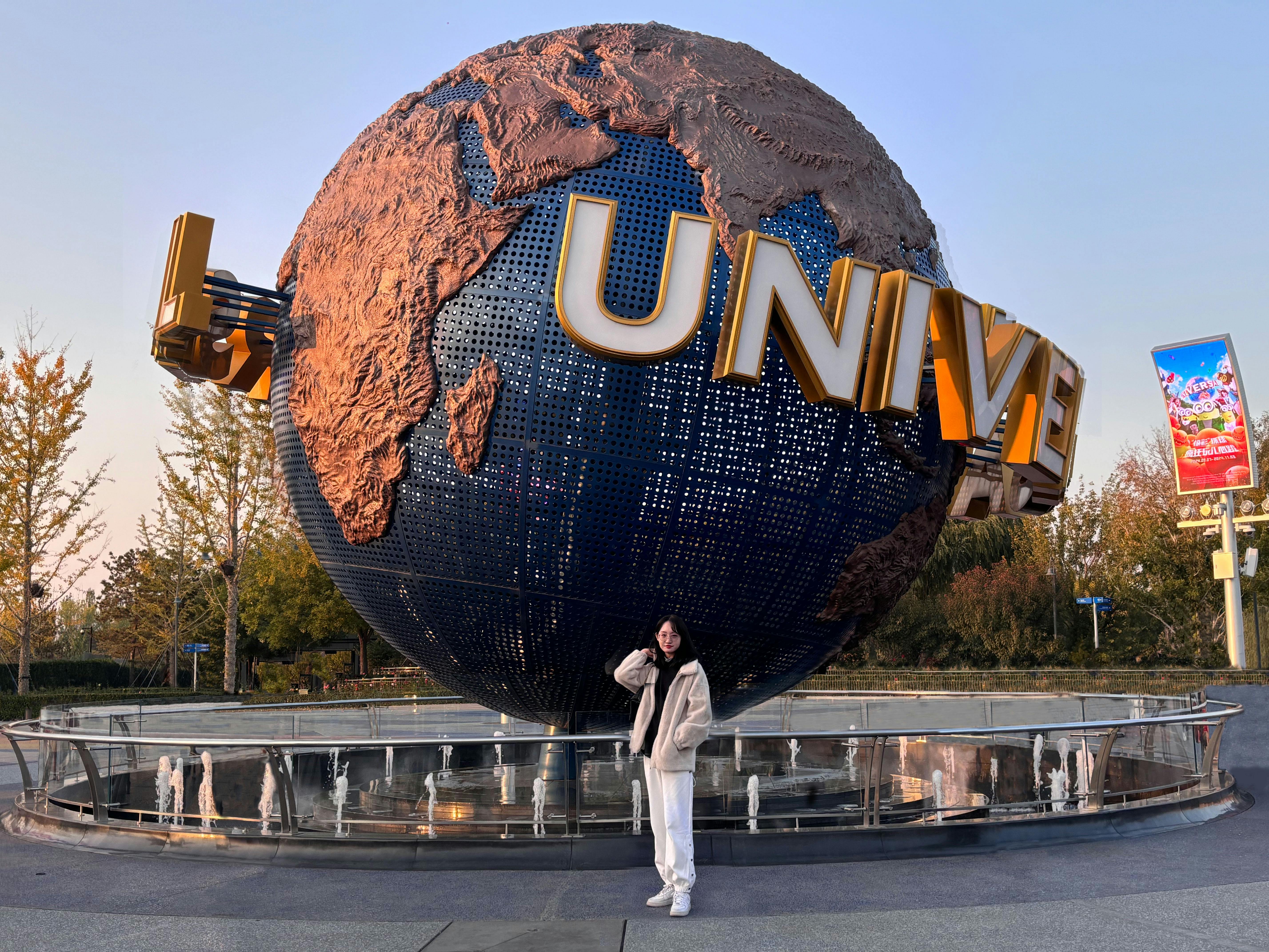 A person poses in front of the iconic Universal Studios globe during sunset.