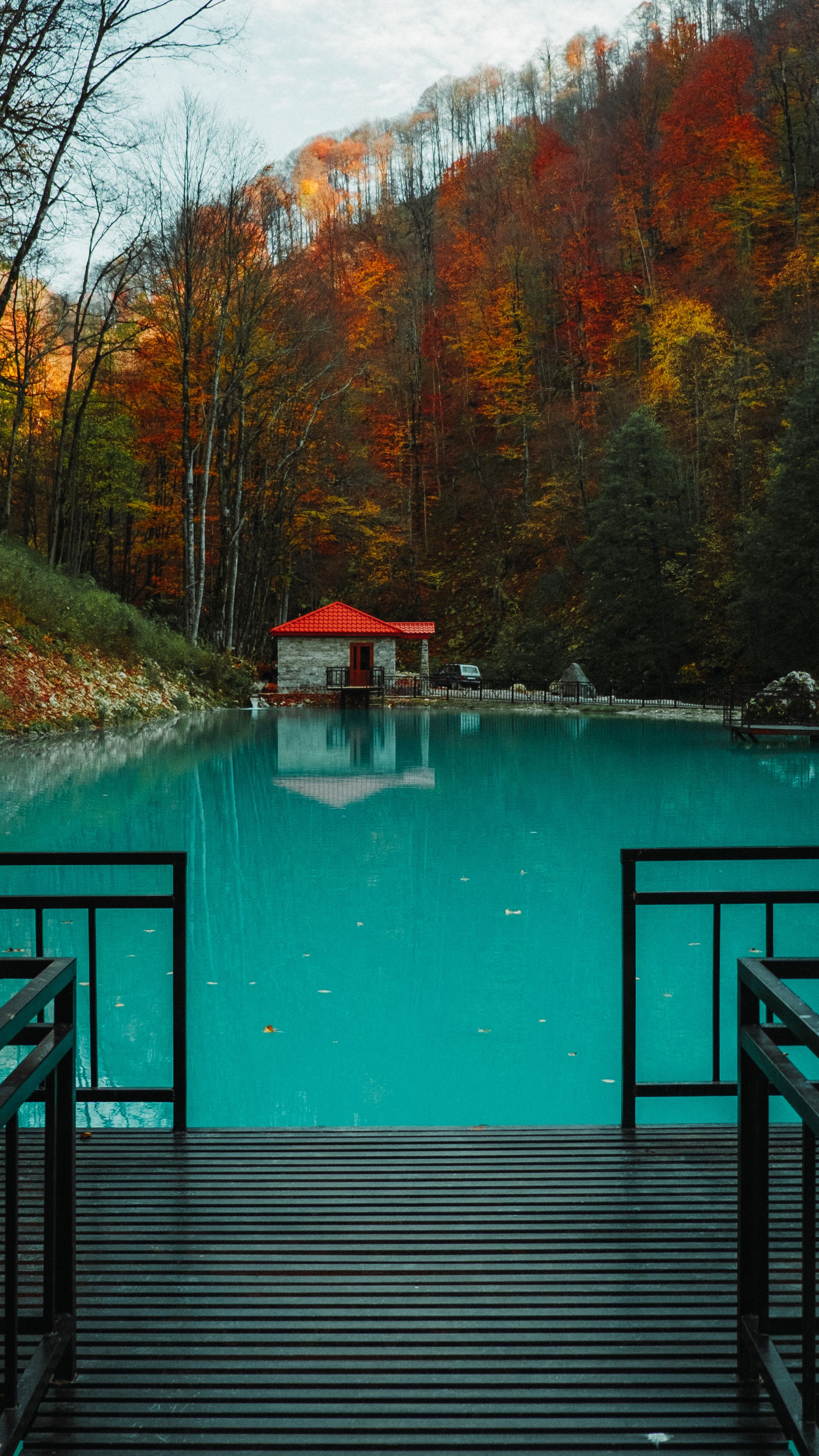 Tranquil lake scene with vibrant autumn trees and a quaint red roof cabin reflected on the water.