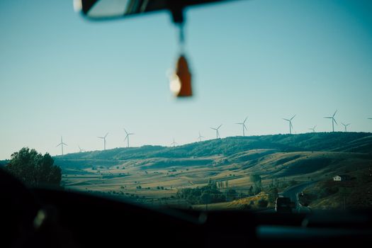 View of expansive landscape with wind turbines from a car window, captured during a drive.