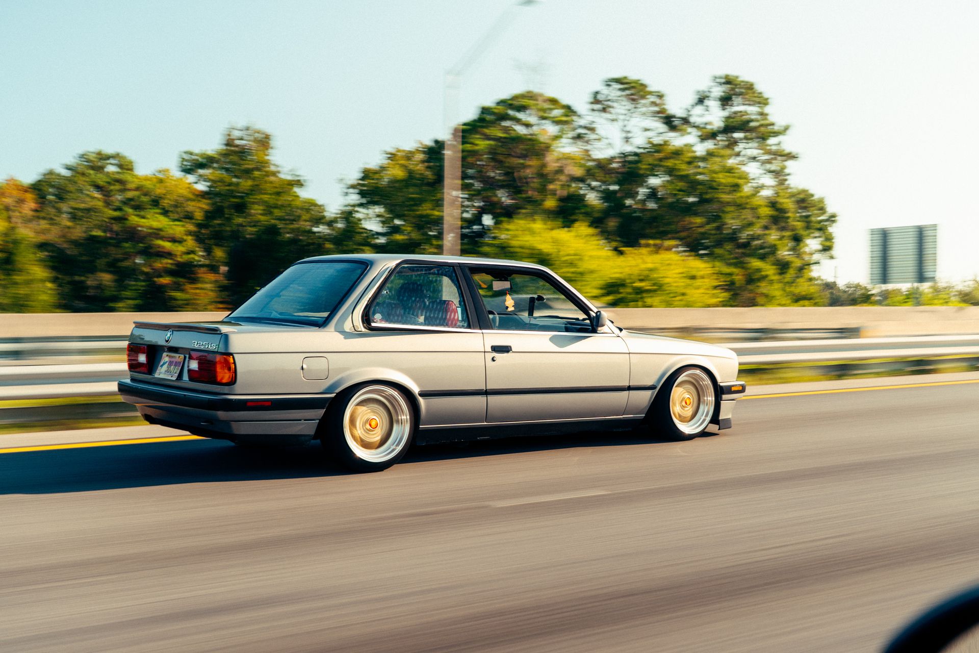 Classic silver car speeding on highway with blurred background and trees.