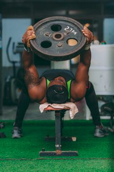 Muscular man lifting weights with a 27 kg plate in an indoor gym setting in Accra, Ghana.