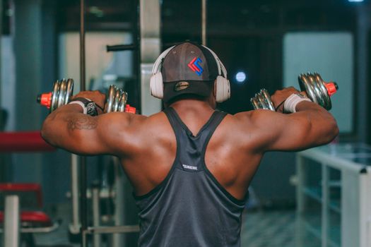 Focused male lifting dumbbells in gym, demonstrating strength and concentration.