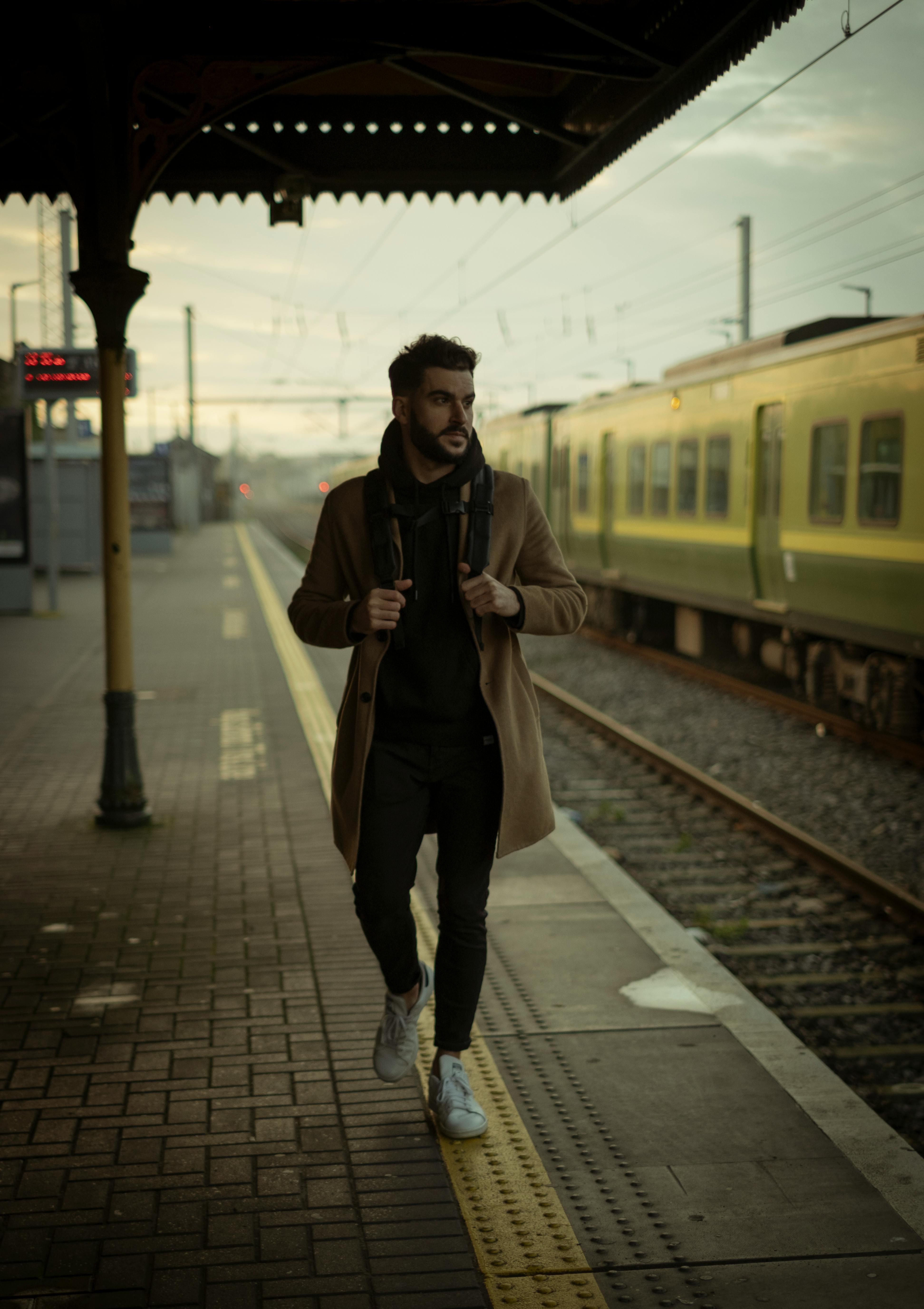 man wearing brown coat walking near train station